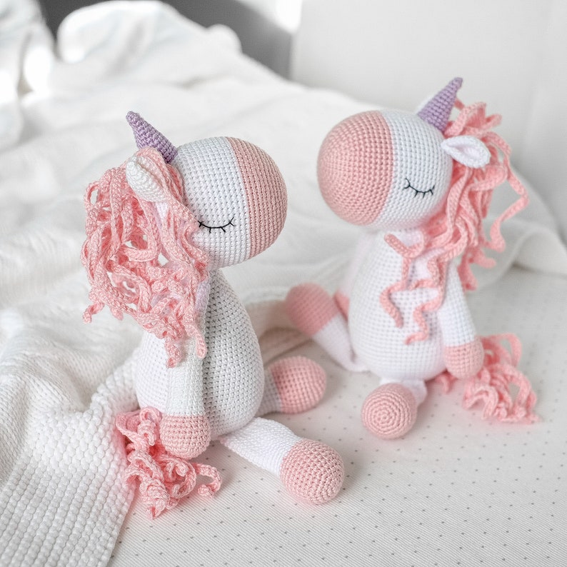 May include: Two crocheted unicorn toys with pink and white yarn. The unicorns have closed eyes and pink yarn for their manes and tails.