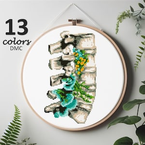 May include: Cross-stitch embroidery art in a wooden hoop. The design features a stylized rib cage with teal and yellow floral accents. The text "13 colors DMC" is displayed in the upper left corner. The artwork is hanging on a white wall.