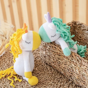 May include: Two crocheted unicorn toys, one with yellow and white yarn and the other with green and white yarn. The unicorns are kissing and are sitting in a wicker basket.