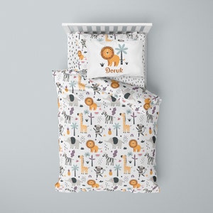 May include: A white and grey children's bedding set with a jungle animal print. The bedding set features a pillowcase with a lion, palm tree, and the name "Doruk".