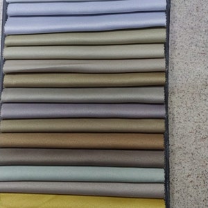 Puede incluir: Un libro de muestras de tela con una variedad de colores, incluyendo blanco, gris, beige, marrón, verde, dorado, morado y azul.