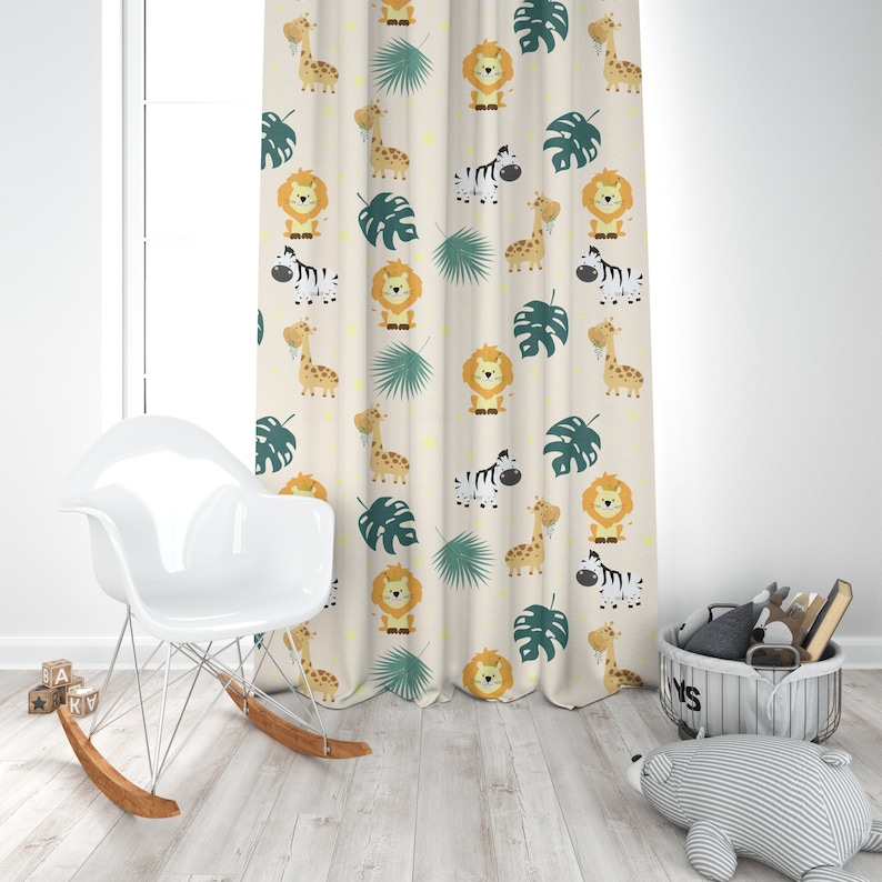 K&ouml;nnte beinhalten: Ein beigefarbener Vorhang mit einem sich wiederholenden Muster aus L&ouml;wen, Zebras, Giraffen und Palmenbl&auml;ttern. Der Vorhang h&auml;ngt in einem Raum mit einem wei&szlig;en Schaukelstuhl und einem grauen Korb aus Weide.