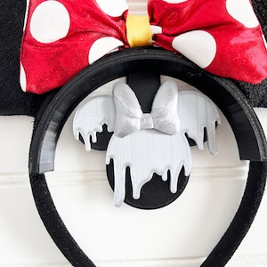 May include: Black headband with a red bow with white polka dots and a silver dripping Mickey Mouse ears design.