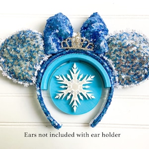 Può includere: Orecchie di Minnie Mouse in paillettes blu e argento con un supporto per fascia per capelli a forma di fiocco di neve bianco. Il supporto per fascia per capelli ha un motivo a fiocco di neve blu. Le orecchie non sono incluse con il supporto per fascia per capelli.