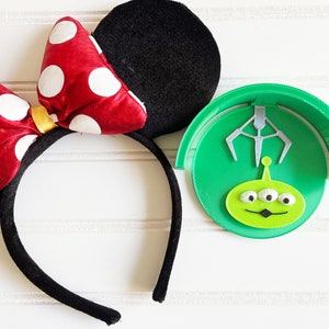 May include: A black headband with a red and white polka dot bow and black mouse ears. A green headband with a three-eyed alien character and a silver claw.