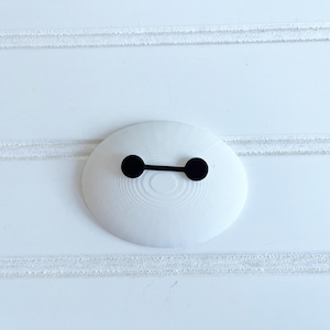 May include: A white, oval-shaped object featuring a black horizontal line and two black circles, reminiscent of a cartoon character's face. The object is set against a white background with horizontal lines.