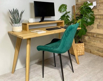 Könnte beinhalten: Ein Holzschreibtisch mit einem grünen Samtstuhl. Der Schreibtisch hat einen Monitorständer und eine Tastatur auf der Oberfläche. Der Stuhl hat schwarze Metallbeine. Der Schreibtisch steht in einem Raum mit einer hellgrauen Wand und einer Holzwand mit einem Schild, auf dem "Today is your day" steht.