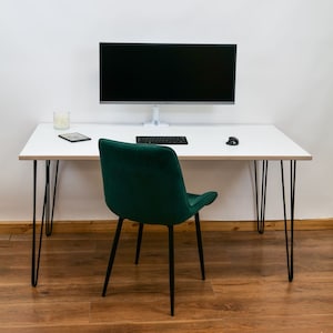 May include: A white desk with hairpin legs and a black computer monitor, keyboard, and mouse. A green velvet chair sits in front of the desk.