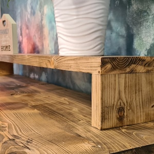 May include: A wooden shelf unit with a natural wood finish. The shelf is mounted to a wooden desk and has a simple design. The shelf is empty and ready to be decorated.