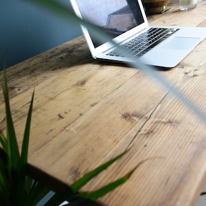 May include: A close-up of a rustic wooden desk with a laptop computer on the surface. The desk is made of reclaimed wood with a natural finish. The laptop is closed and has a silver finish.
