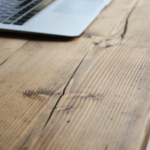 May include: A close-up of a rustic wooden table surface with a laptop computer in the background.