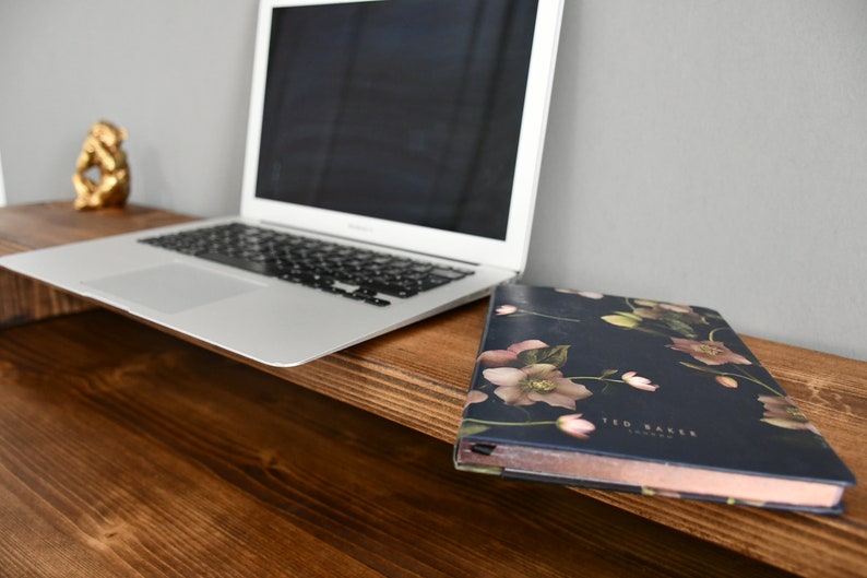 May include: A wooden desk with a laptop computer and a floral notebook on top. The notebook has the text "Ted Baker London" printed on the cover.
