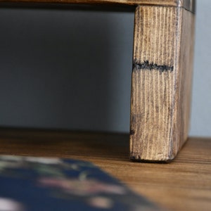 May include: A wooden stand with a dark brown stain. The stand has a rectangular top and a raised base. The stand is made of natural wood with visible grain.