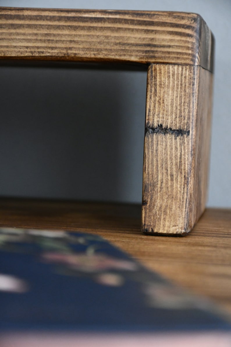 May include: A wooden stand with a dark brown stain. The stand has a rectangular top and a raised base. The stand is made of natural wood with visible grain.