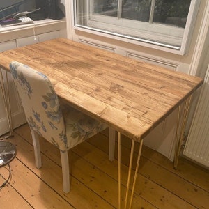 May include: A wooden desk with a natural finish and gold hairpin legs. A floral patterned chair is positioned next to the desk.