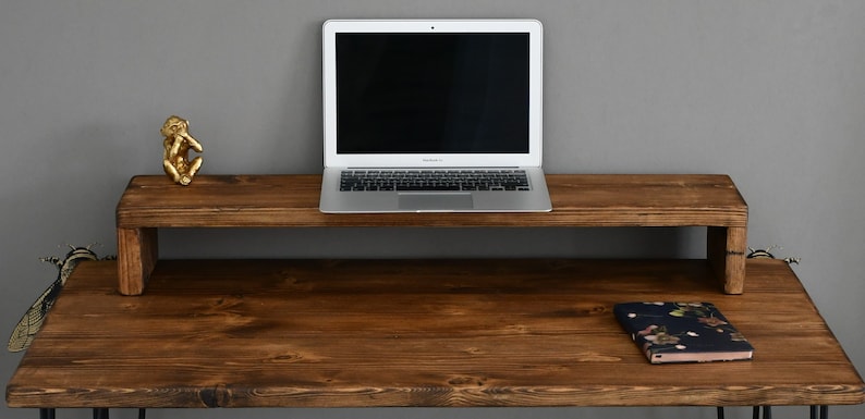 May include: A wooden laptop stand with a dark brown finish sits on a matching wooden desk. A silver laptop is on the stand, and a small gold monkey figurine is on the desk.