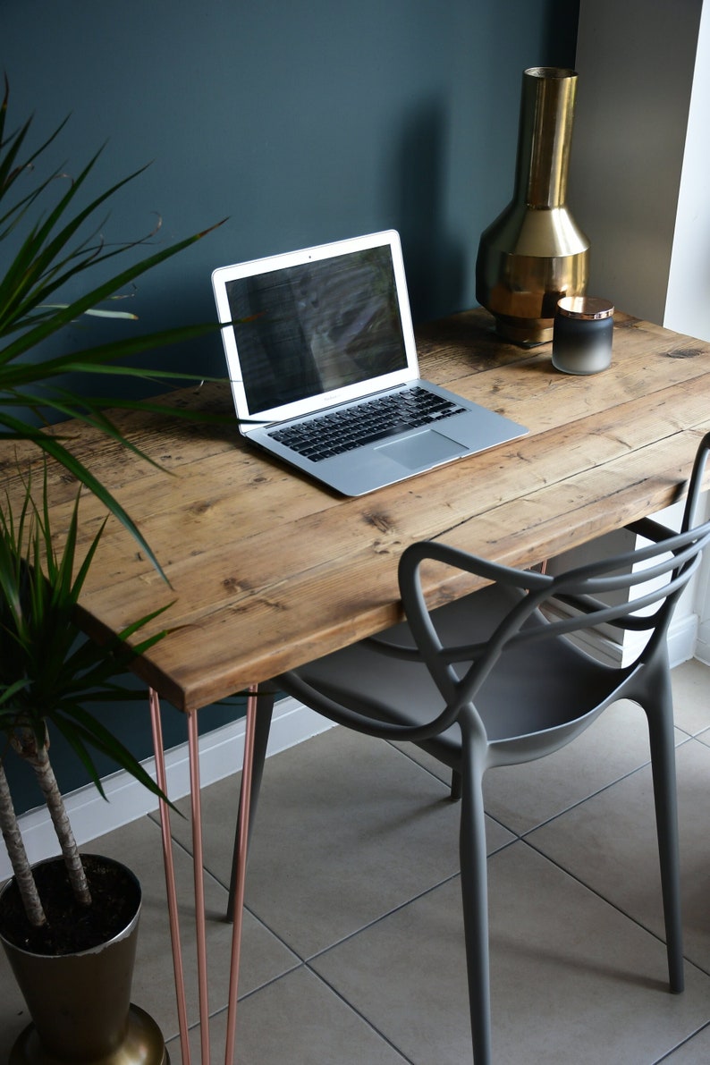 May include: A rustic wooden desk with copper hairpin legs, a laptop computer, a gray chair, and a gold vase with a black candle on top.