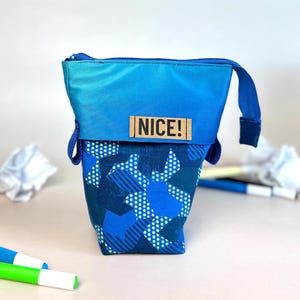 Könnte beinhalten: Eine blaue und grüne Reißverschlusstasche mit geometrischem Muster. Die Tasche hat einen blauen Griff und ein braunes Etikett mit der Aufschrift "NICE!"