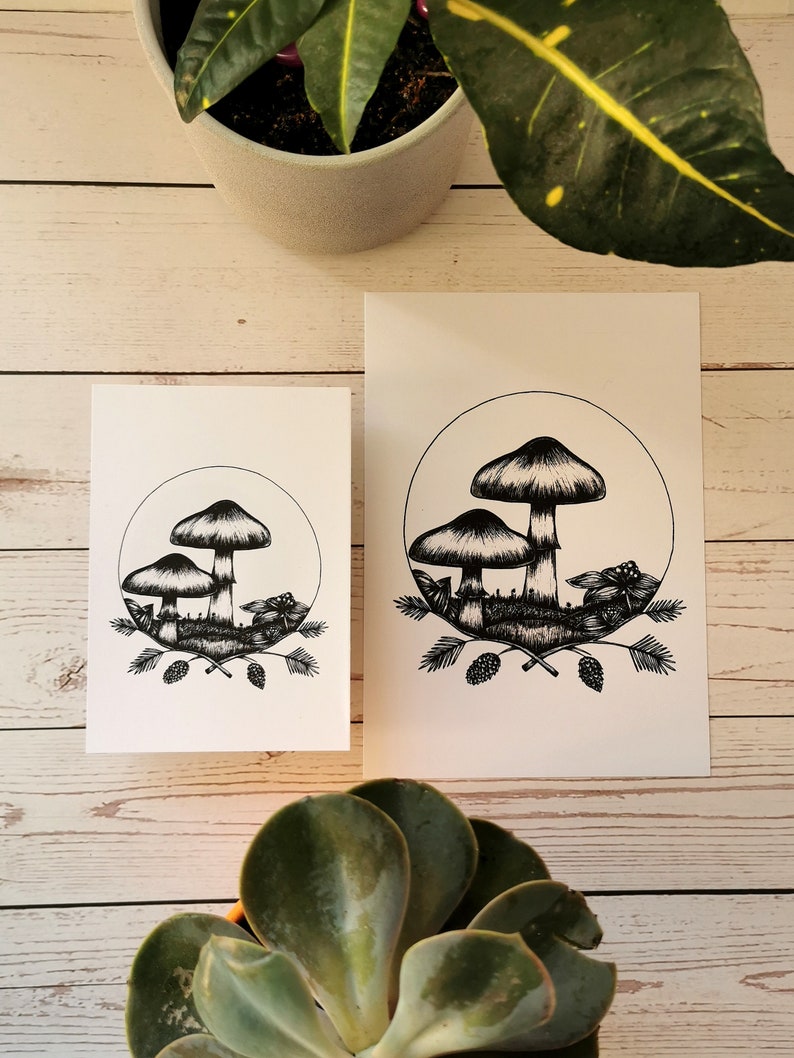 May include: Two black and white prints of mushrooms with pine cones and branches. The prints are on white card stock and are framed with a white border.