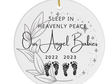 May include: White ceramic ornament with a gray floral design and the text "Sleep in Heavenly Peace Our Angel Babies 2022 2023".  The ornament features three sets of gray baby footprints.