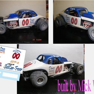 May include: A white and blue model car with the number "00" on the side. The car is a modified 1930s coupe with a blue roof and a white body. The car has a red "Dover Brake" logo on the side. The car is sitting on a black surface. The car is built by Mick Wetzel.