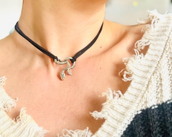 May include: A black choker necklace with a silver snake pendant. The necklace is worn by a person with short dark hair.
