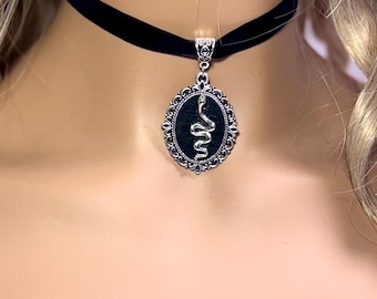 May include: A black velvet choker necklace with a silver pendant featuring a snake design in a black oval frame.