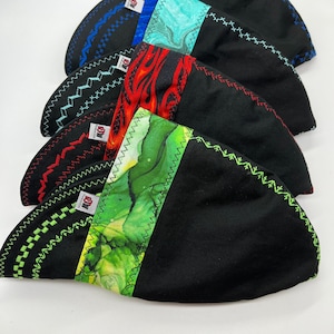 May include: Five welding caps with different patterned fabric panels. The caps are black with a zig-zag stitch around the edges. The fabric panels are blue, green, red, and green. Each cap has a red label with the text "DM"