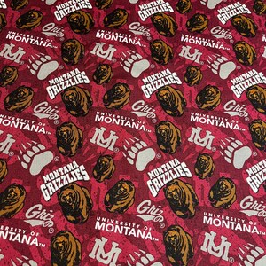 May include: A red fabric with a repeating pattern of a brown bear, a paw print, and the text "University of Montana" and "Montana Grizzlies".