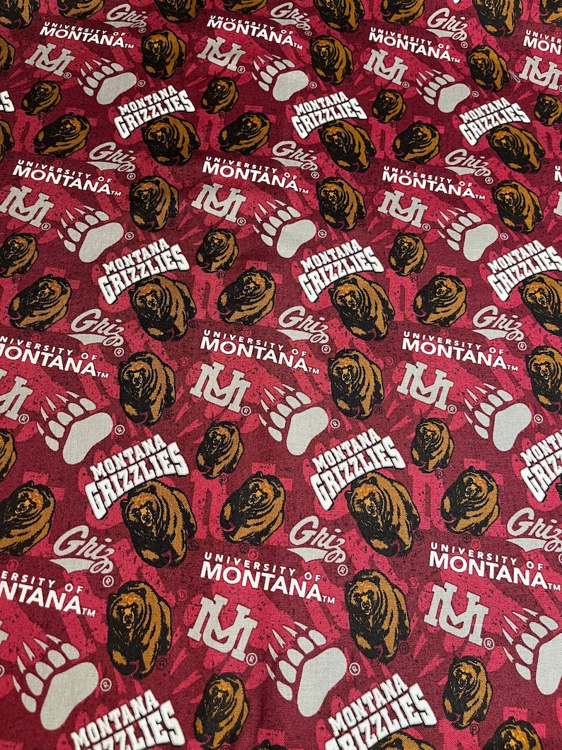 May include: A red fabric with a repeating pattern of a brown bear, a paw print, and the text "University of Montana" and "Montana Grizzlies".