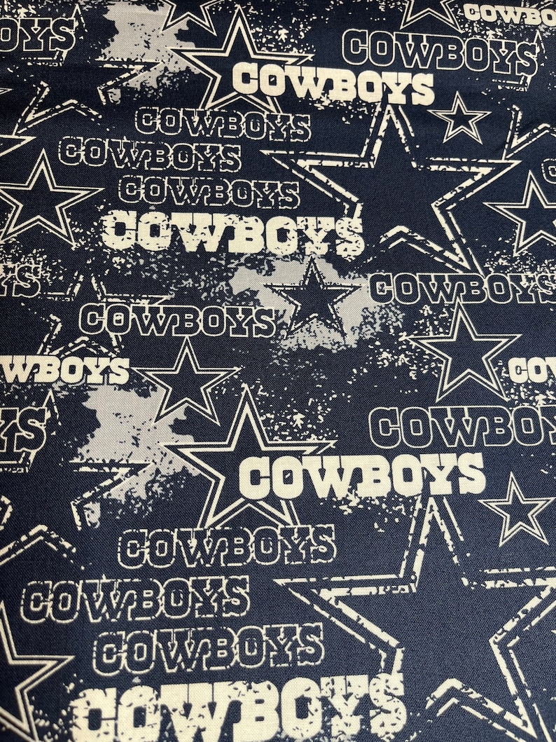 May include: A navy blue fabric with a white distressed pattern of stars and the word "COWBOYS" repeated throughout.