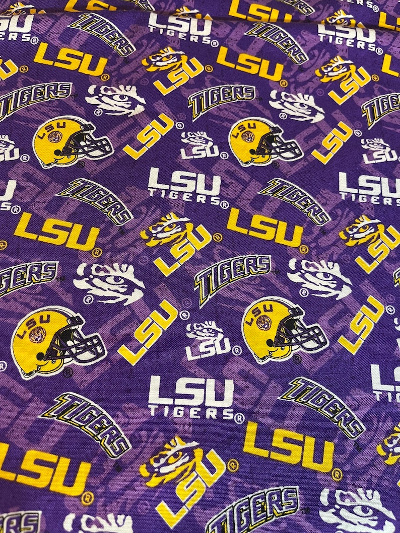 May include: Purple fabric with a repeating pattern of the LSU Tigers logo in yellow and white. The logo includes the words "LSU Tigers" and a tiger head.