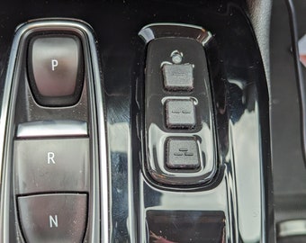 May include: Close-up of a black car's gear shift with buttons for "P", "R", "N", and "OFF".