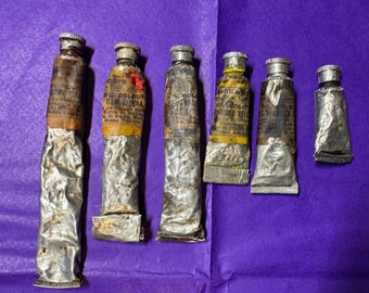 May include: Six vintage oil paint tubes with labels, in various states of wear, against a purple background. The tubes are silver with brown and yellow labels. The paint tubes are of different sizes.