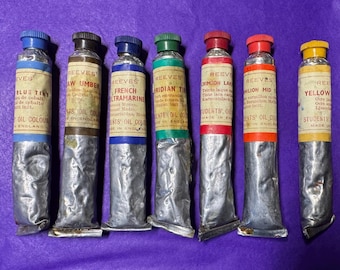 May include: A collection of seven vintage Reeves oil paint tubes, each with a different color, including blue, raw umber, French ultramarine, and yellow. The tubes have labels with text and are made in England.