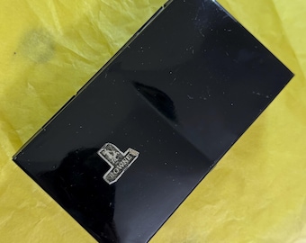 May include: A black rectangular box with a silver emblem that reads "TOWNES". The box is on a yellow surface. The box has a glossy finish and appears to be made of a sturdy material.