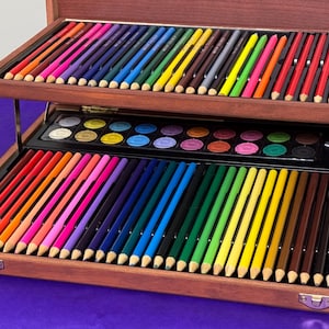 May include: A wooden art set with a variety of colored pencils and watercolor paints. The set is open, revealing multiple rows of vibrant pencils in various colors, and a selection of watercolor paints. The set is on a purple surface.