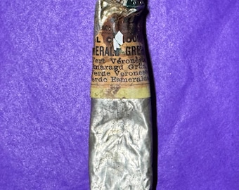 May include: A vintage, partially used tube of emerald green artist's paint. The metal tube is crumpled and shows signs of age, with text in multiple languages. The cap is silver, and the label displays the name "Emerald Green".