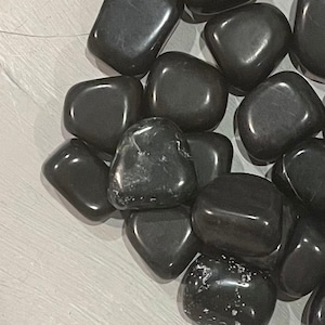 Op de afbeelding: Een verzameling gladde, zwarte, getrommelde stenen. De stenen zijn van verschillende grootte en vorm, sommige vertonen subtiele witte aderen.