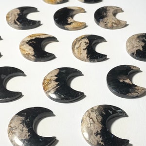 May include: A collection of 12 black and white agate crescent moon shaped stones. The stones have a natural, organic pattern and are polished smooth.