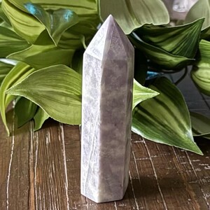 May include: A light purple amethyst crystal point with a smooth, polished finish. The crystal is shaped like a point and has a natural, cloudy appearance.