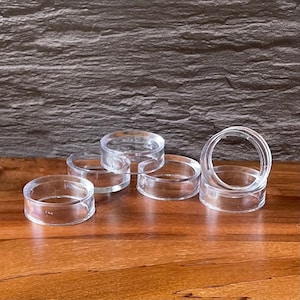 May include: Six clear plastic napkin rings, stacked and arranged on a wooden surface.
