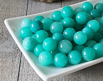 May include: A white ceramic dish filled with smooth, round, teal green jade stones.
