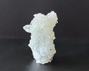 Puede incluir: Un grupo de formaciones de cristales azul claro. Los cristales tienen una superficie rugosa y texturizada y están agrupados verticalmente. Los cristales son translúcidos, permitiendo el paso de la luz.