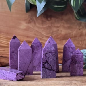 May include: A collection of purple crystal towers with a marbled appearance. The crystals are various sizes and shapes, with pointed tops and a rectangular base. The crystals are arranged on a wooden surface.