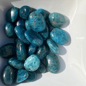 May include: A collection of smooth, polished blue apatite tumbled stones. The stones are various sizes and shapes, with a light blue to dark blue colour.