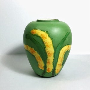 May include: A green ceramic vase with a stylized floral design. The vase features yellow and green painted flowers.
