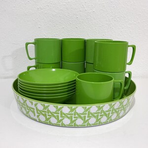 May include: A set of bright green plastic mugs and bowls arranged inside a large round serving tray. The tray features a white and green geometric lattice pattern around its exterior. The mugs have simple handles and a smooth, solid finish.