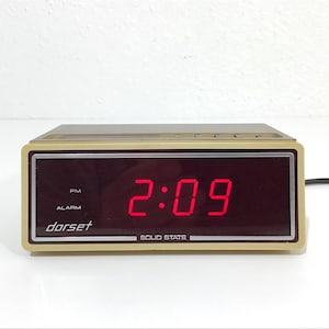 May include: A vintage Dorset digital alarm clock displaying 2:09 PM in bright red numerals. The clock has a beige and brown casing with the word "dorset" printed on the face. The words "ALARM" and "SOLID STATE" are also visible.