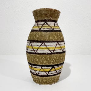 May include: A ceramic vase with a textured, mottled olive-green finish. The body features horizontal bands of dark brown, white, and bright yellow, with a repeating geometric triangle pattern encircling the midsection and lower portion.